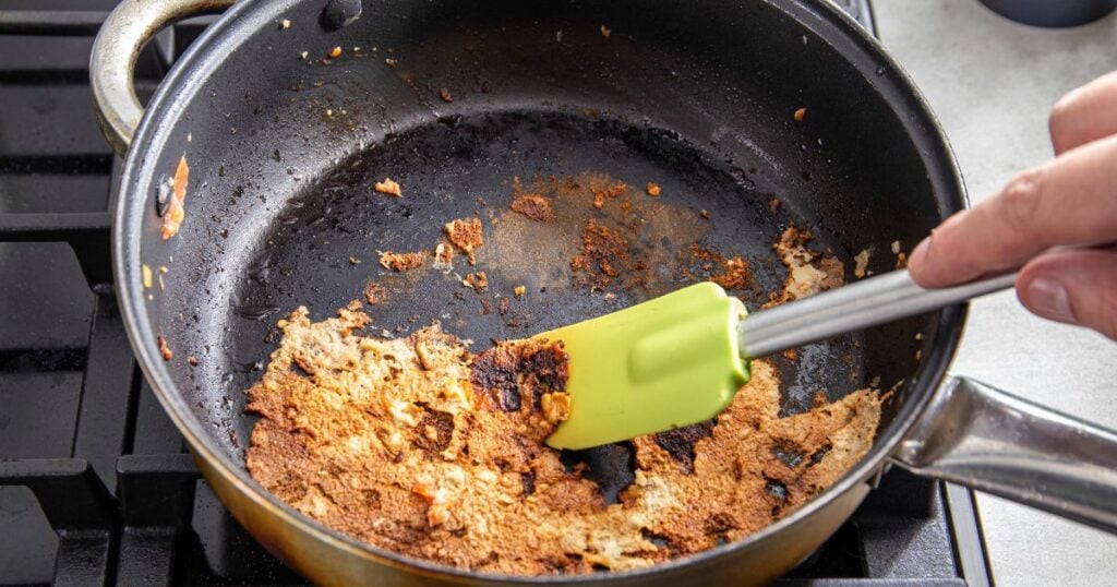 A spatula for stirring food picks off burnt food in a pan. Poor quality Teflon coated pans. Close-up