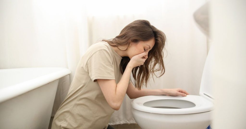 morning sickness experienced by a pregnant woman. She is vomiting near the toilet seat. 